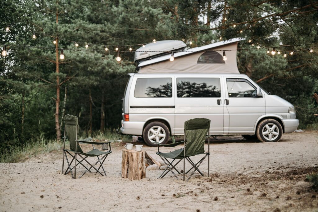Tranquil forest campsite featuring a van, chairs, and string lights.